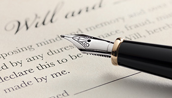 A close-up of a fountain pen resting on a document with the word ''Will'' clearly visible, suggesting a last will and testament
